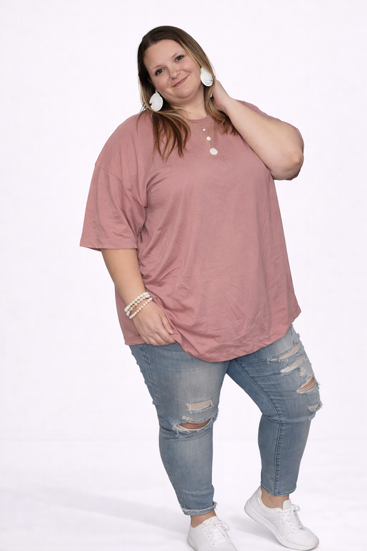 Woman wearing a light pink shirt and ripped jeans on a white background