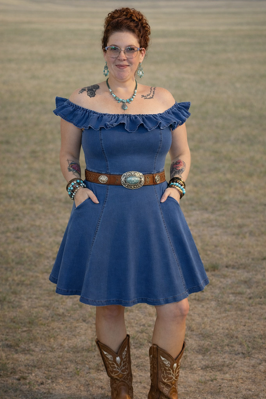 Woman wearing a blue dress with ruffled neckline and brown belt, standing in a field.