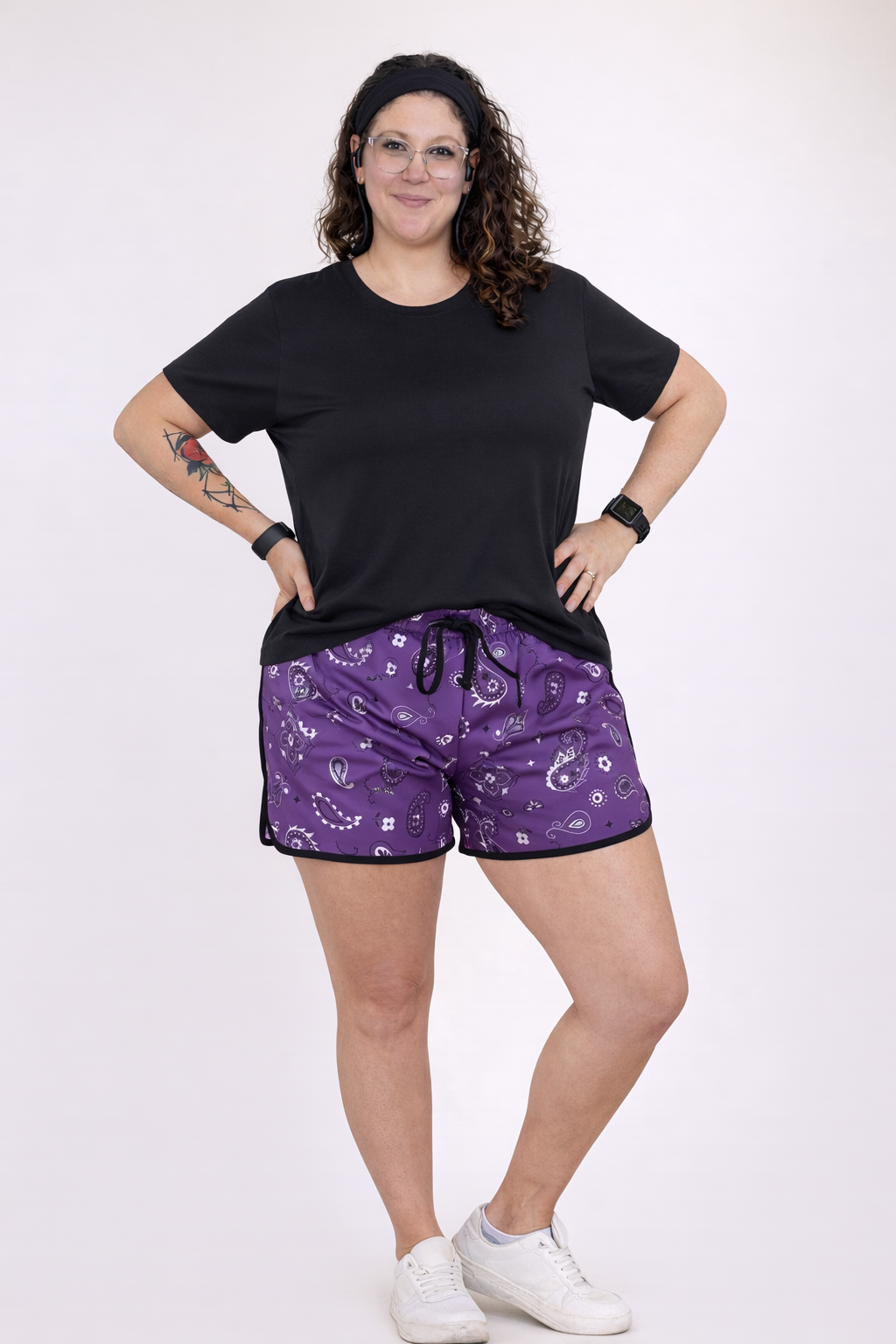 Person wearing a black t-shirt and purple bandana patterned shorts on a white background