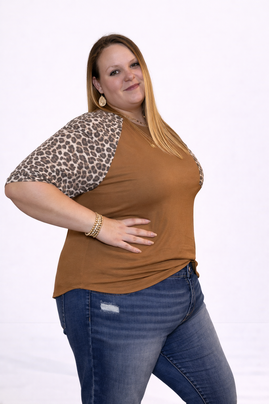 Woman wearing a brown top with leopard print sleeves and blue jeans on a white background
