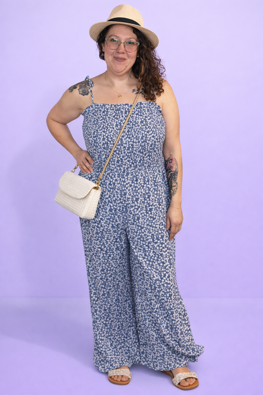 Woman wearing a floral romper and hat against a purple background