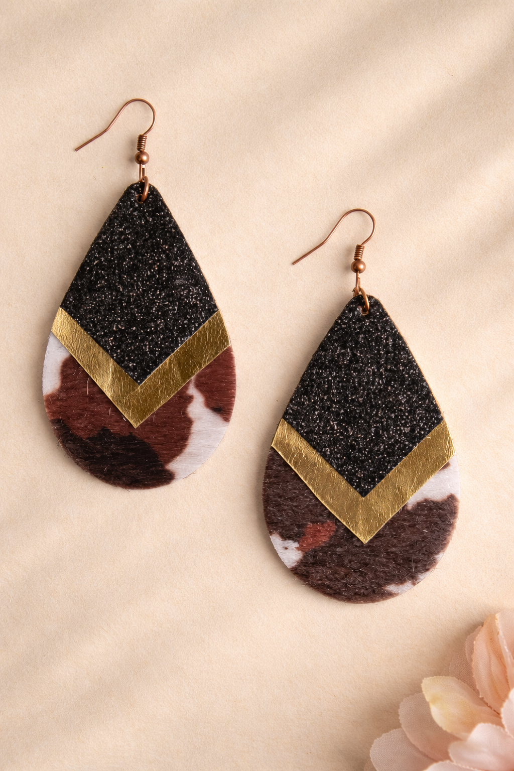 Teardrop-shaped earrings with black, gold, and brown design on a beige background