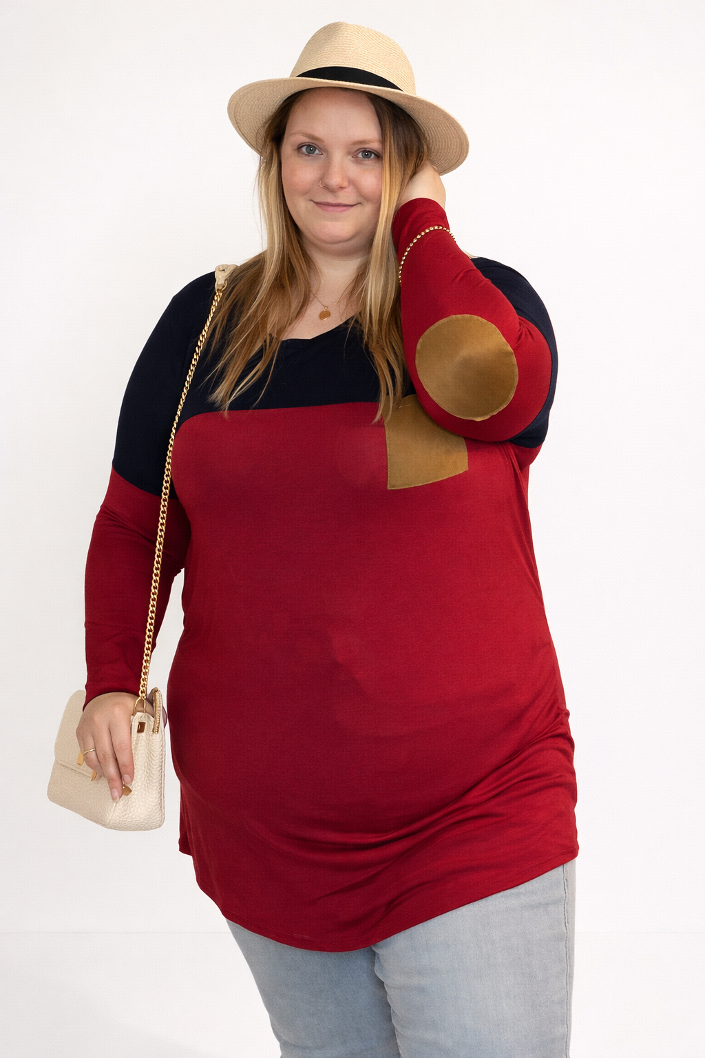Woman wearing a red dress with black and gold accents, holding a beige hat.