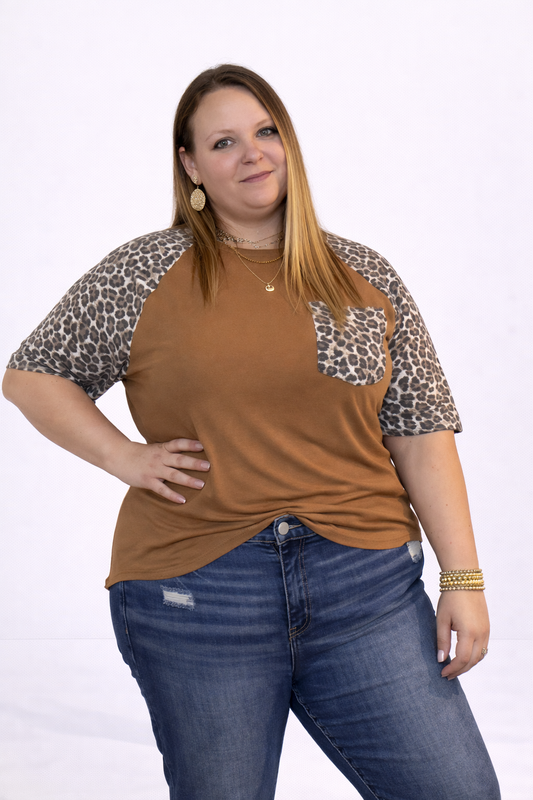 Woman wearing a brown shirt with leopard print sleeves and blue jeans on a white background