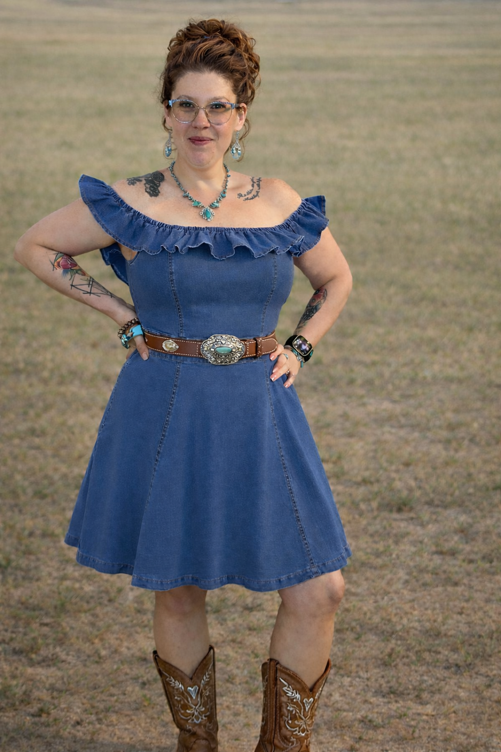 Woman wearing a blue dress with ruffled sleeves and cowboy boots standing in a field.