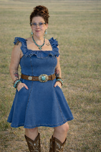 Woman wearing a blue dress with ruffled sleeves and a brown belt, standing in a field.