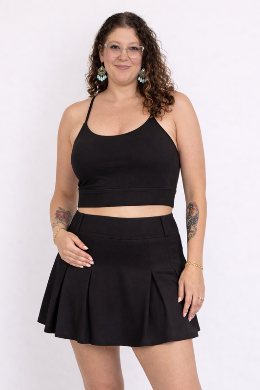 Woman wearing a black crop top and black skort on a white background