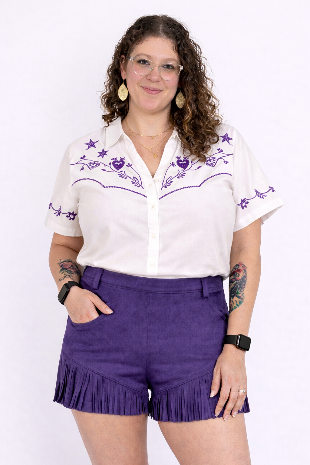 Woman wearing a white blouse with purple embroidery and purple shorts with fringe on a white background