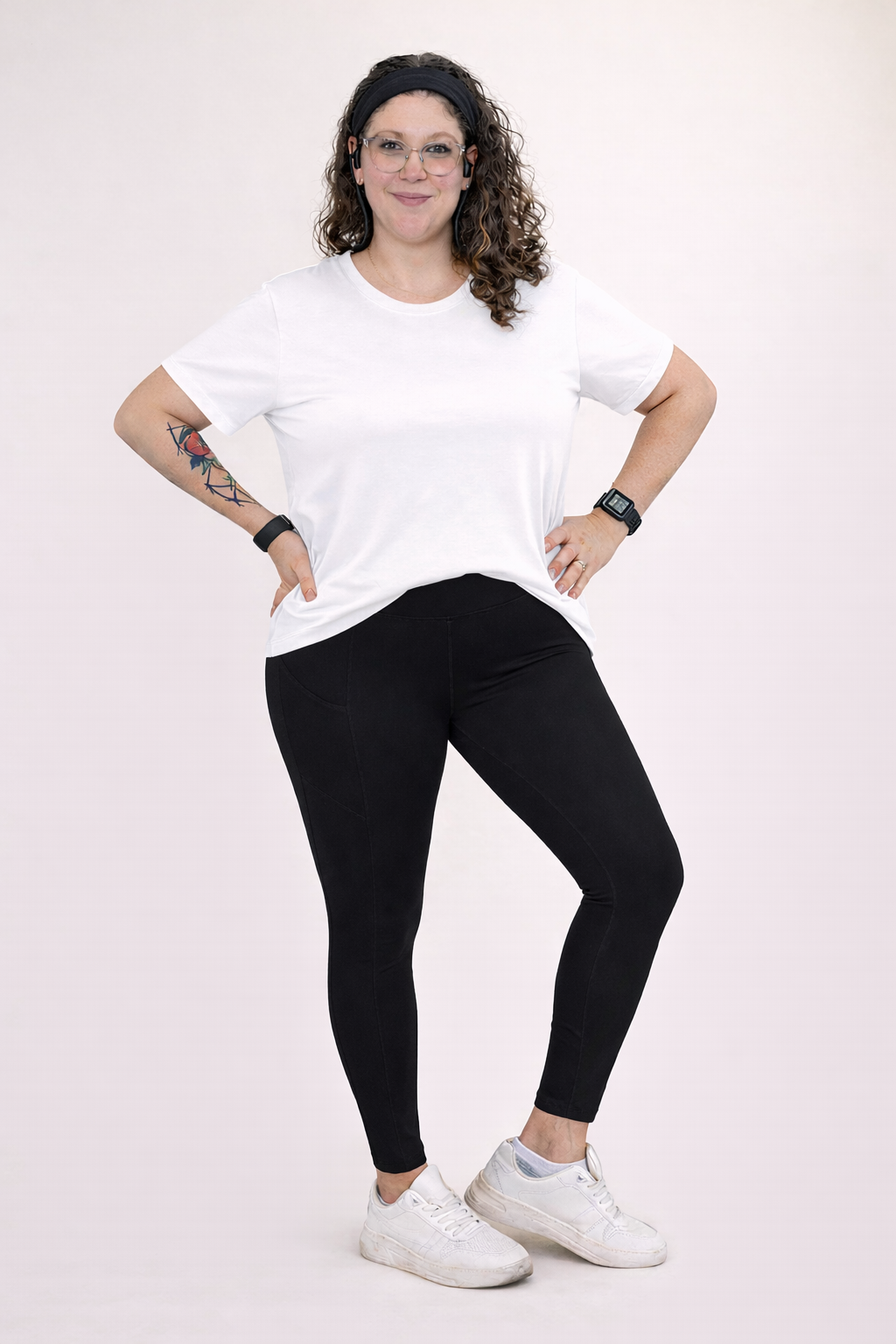 Woman wearing black leggings and a white top against a khaki background. 