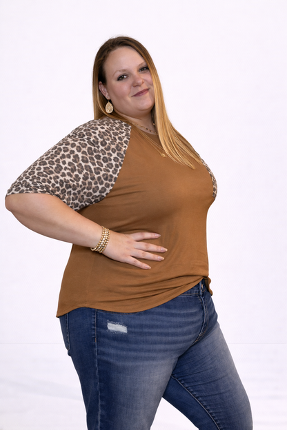 Woman wearing a brown top with leopard print sleeves and blue jeans on a white background