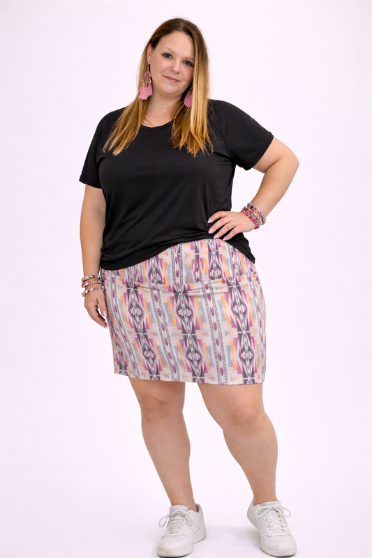 Woman wearing a multi-colored printed skirt and black shirt with a white background. 