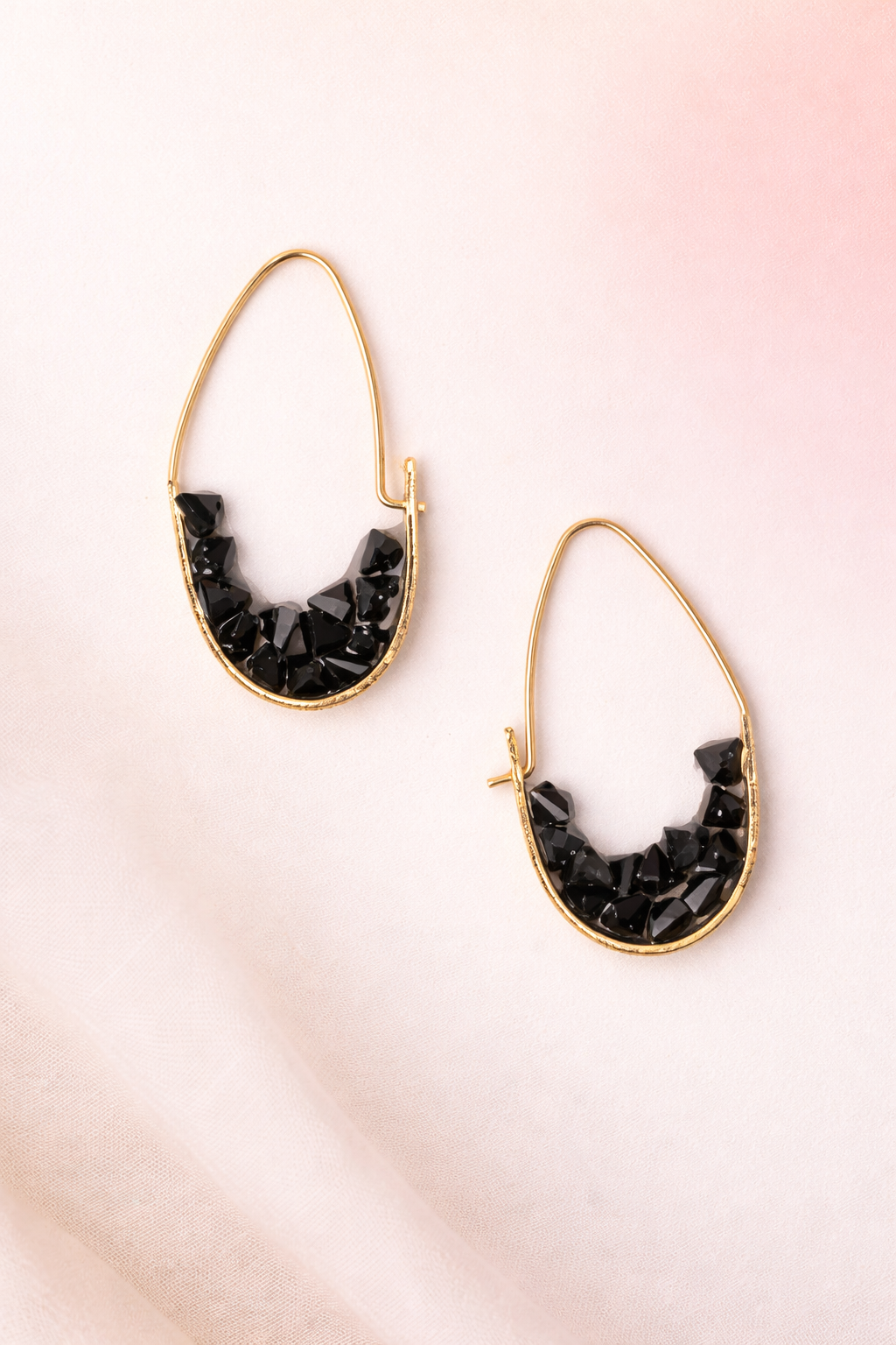 Gold hoop earrings with black stone accents on a pink gradient background