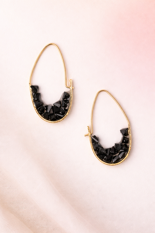 Gold hoop earrings with black stone accents on a pink gradient background
