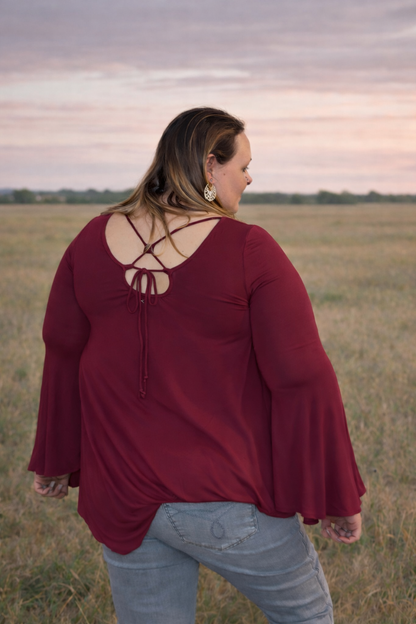 Woman wearing a burgundy blouse with a unique back design in an open field.