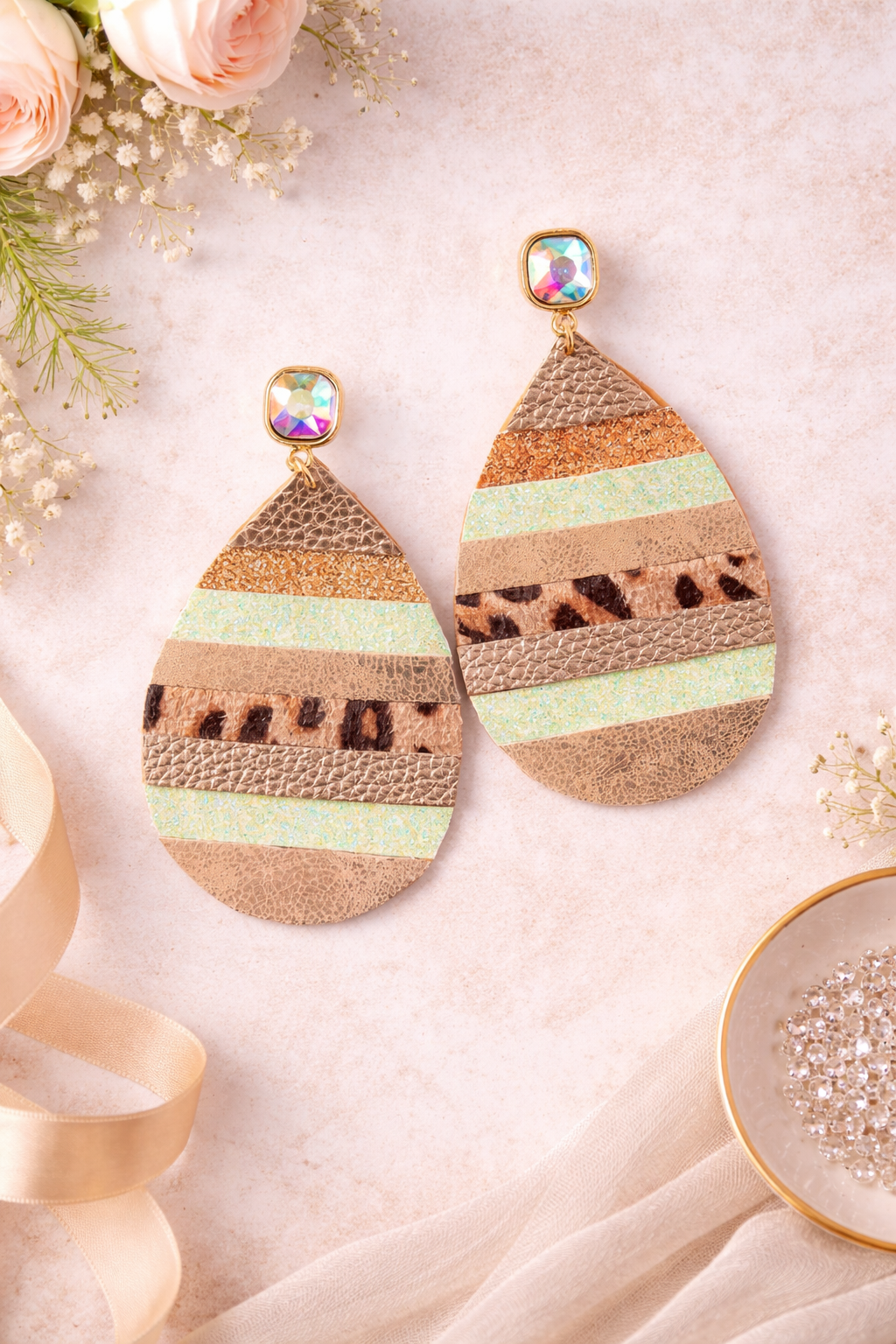 Teardrop-shaped earrings with striped pattern on a soft surface with flowers and ribbons.