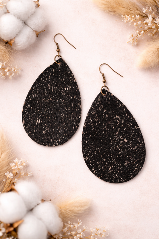 Black fur teardrop earrings on a soft white background with cotton and dried flowers.