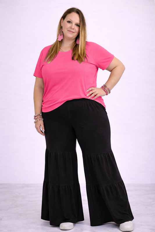 Woman wearing a pink top and black tiered pants on a white background